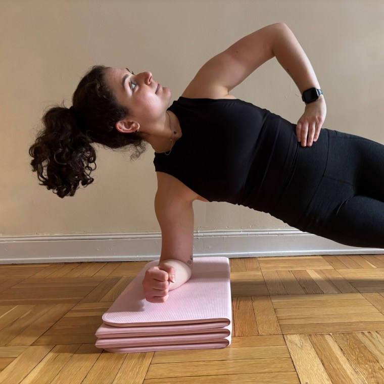 A woman doing a side plank while elevating her arm on a pink Stakt Mat.