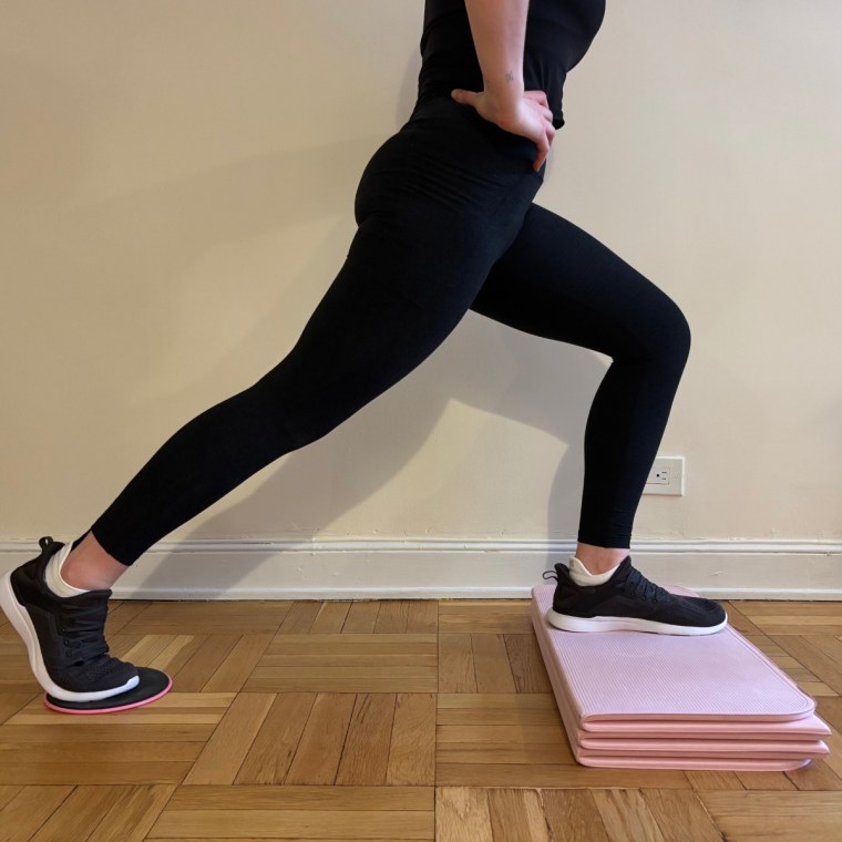 A woman doing a lunge with a slider underneath her back foot and her front foot elevated on a pink Stakt Mat.