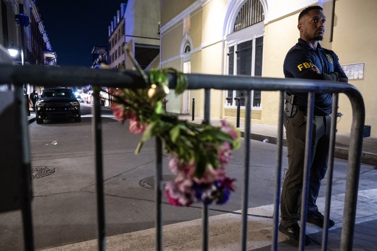 A member of the FBI looks on near a bouquet of flowers tied to a fence, a block from Bourbon Street, after at least 15 people were killed during an attack early in the morning on January 1, 2025 in New Orleans, Louisiana. 