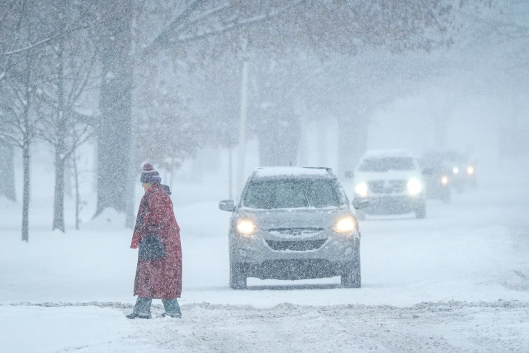 A pedestrian crosses the street as cars wait during a blizzard