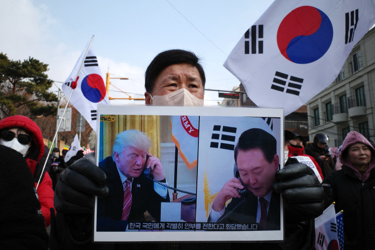 Un partidario del presidente surcoreano, Yoon Suk-yeol, sostiene un cartel de Yoon y del presidente entrante de Estados Unidos, Donald Trump, que traduce "Respondió enviando un saludo especial al pueblo de Corea del Sur."Durante una manifestación cerca de su residencia en Seúl el 6 de enero de 2025.