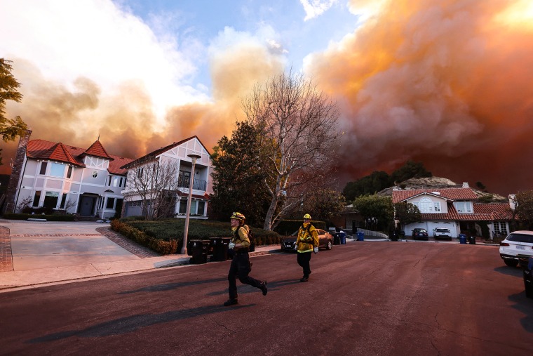  Firefighters run as a brush fire burns in Pacific Palisades, Calif., on Jan. 7, 2025.