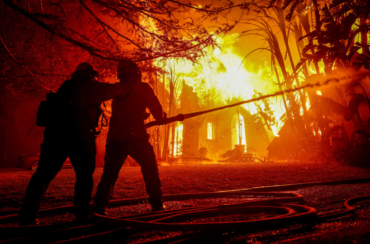 Firefighters spray water on a burning home.