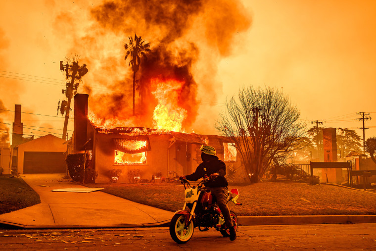 A motorcyclist stops to look at a burning home during the Eaton fire