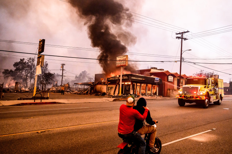 Image: Residents ride their motorbike past a burning liquor store