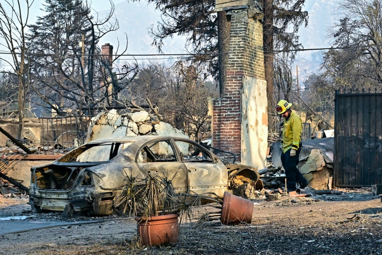 A firefighter inspects destruction next to a burnt car.