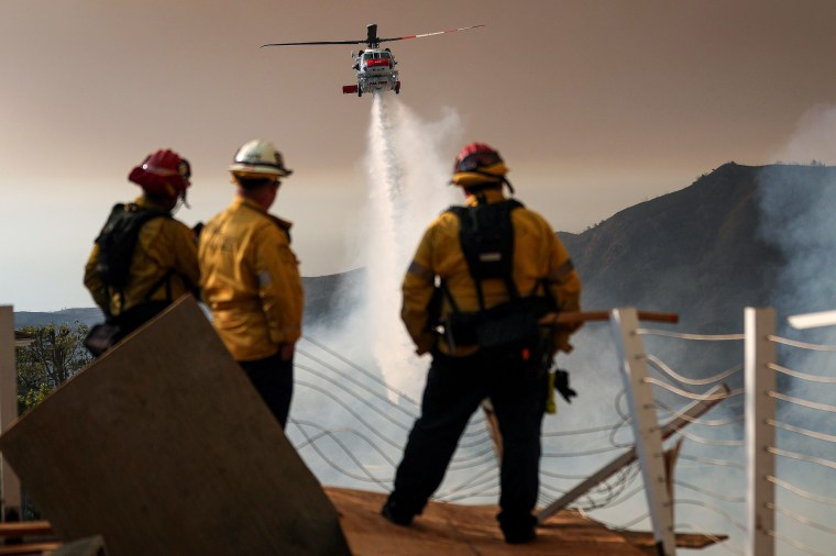 A firefighting helicopter drops water on the Palisades Fire.