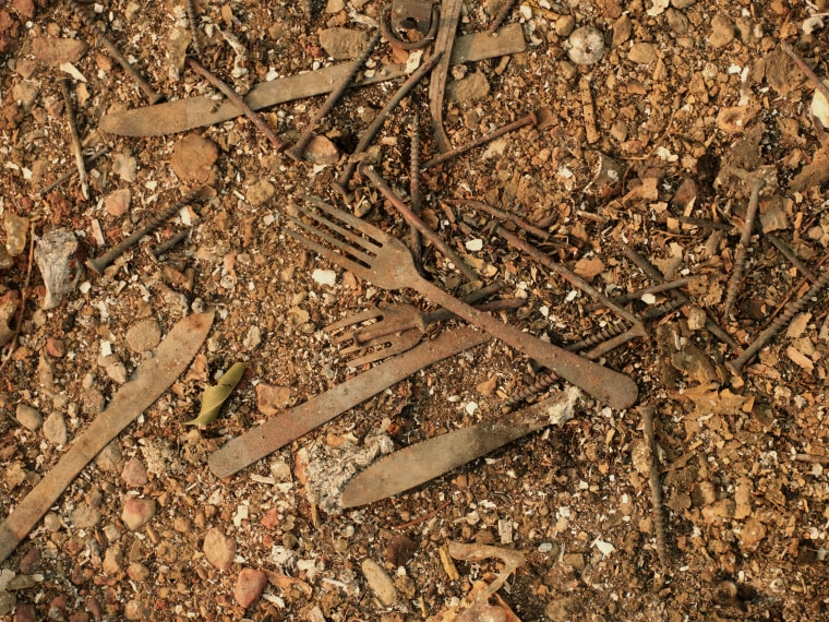 Forks and knives, charred, amongst dirt and rubble.