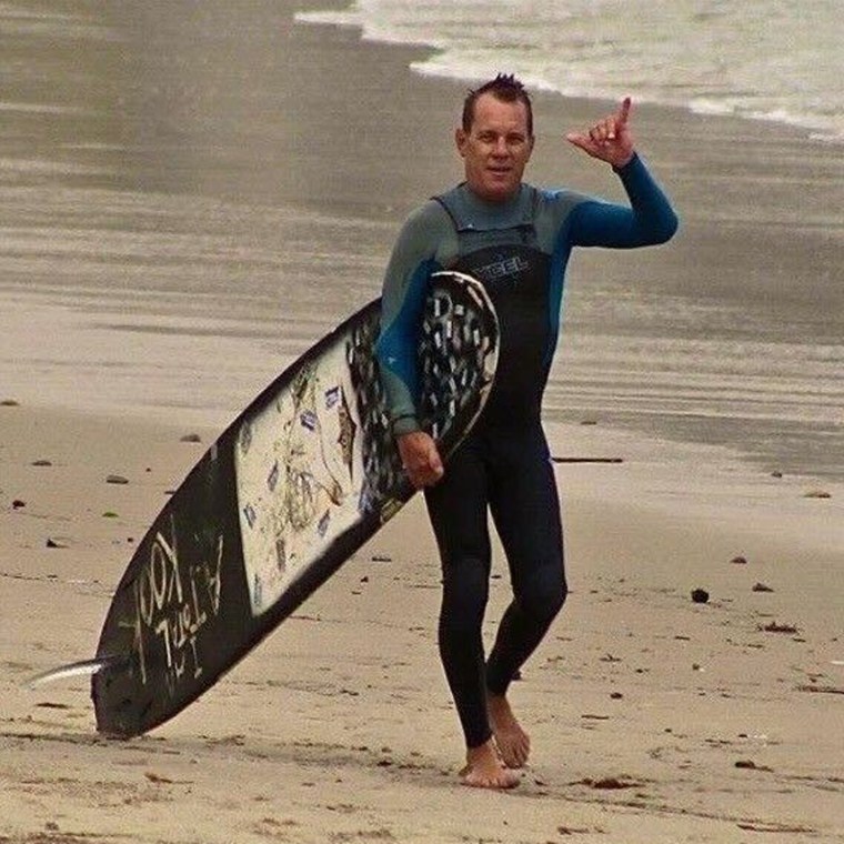 Randall Miod walks on the beach with a surfboard