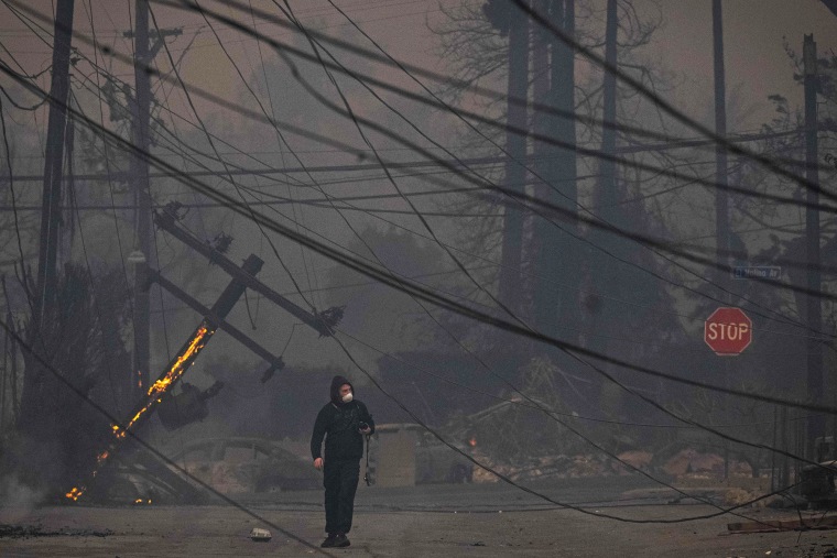 A man walks through Altadena's business district through downed power lines on Jan. 8, 2025.