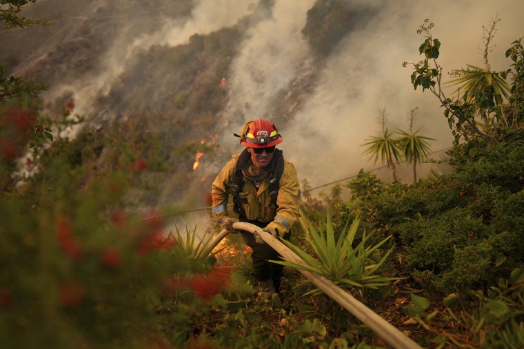 A firefighter sets up a hose while battling the Palisades Fire in Mandeville Canyon on Saturday, Jan. 11, 2025, in Los Angeles.