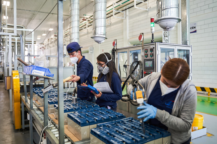 Trabajadores enmascarados sueldan baterías ácidas en una fábrica.