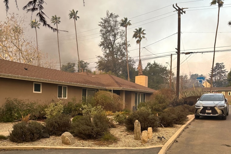 A home is pictured outside on a street with smoke in the sky above