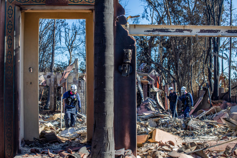 Firefighters inspect a burned house in the middle of debris.