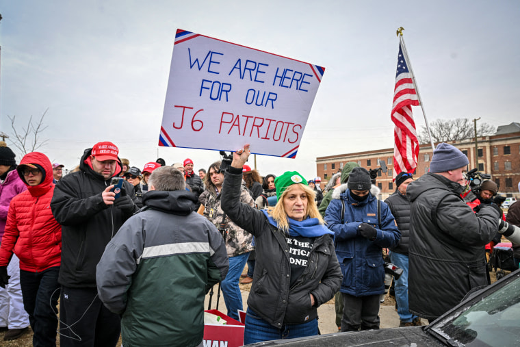 Sandy Weir with a sign that reads" WE ARE HERE FOR OUR J6 PATRIOTS."