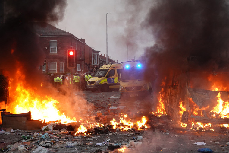 2024年7月30日、イギリスのサウスポートで、炎上する警察車両の近くでデモ参加者を制止する機動隊。 