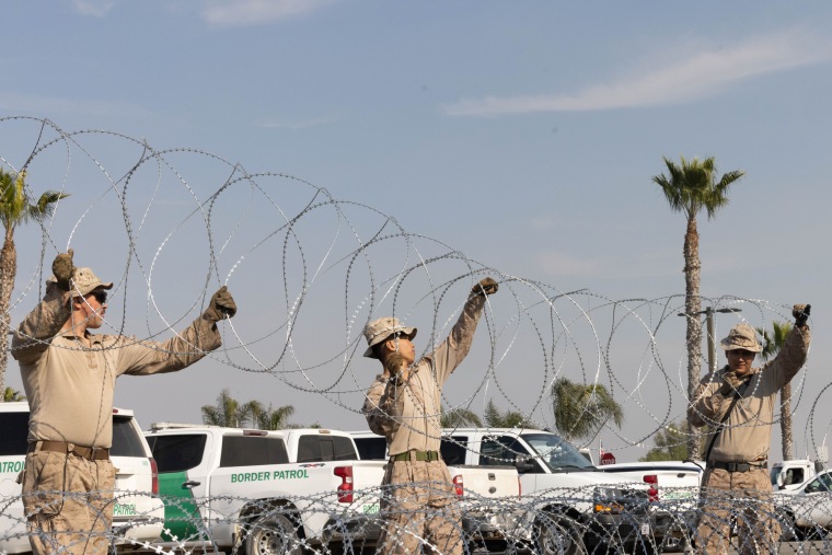 Three people hold barbed wire up