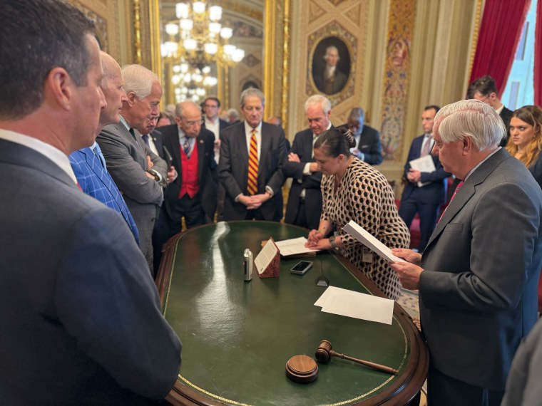 People crowd around a table as a woman votes on a document