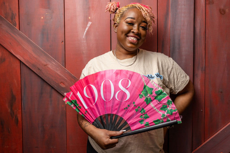 Alexus Sumpter holds a pink fan that reads "1908"