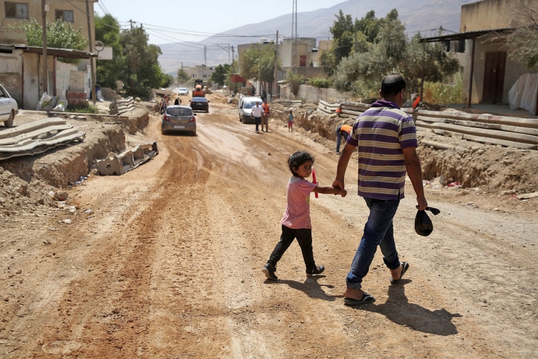 Um pai e sua filha atravessam uma rua sob reformas como parte de uma doação da USAID na Cisjordânia ocupada em 2018. 