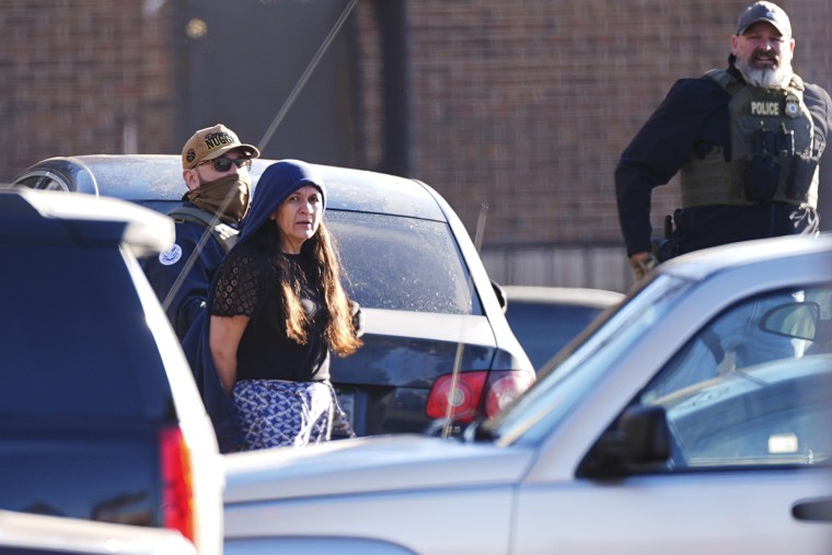 Law officials escort a woman out of an apartment complex during a raid in Denver.