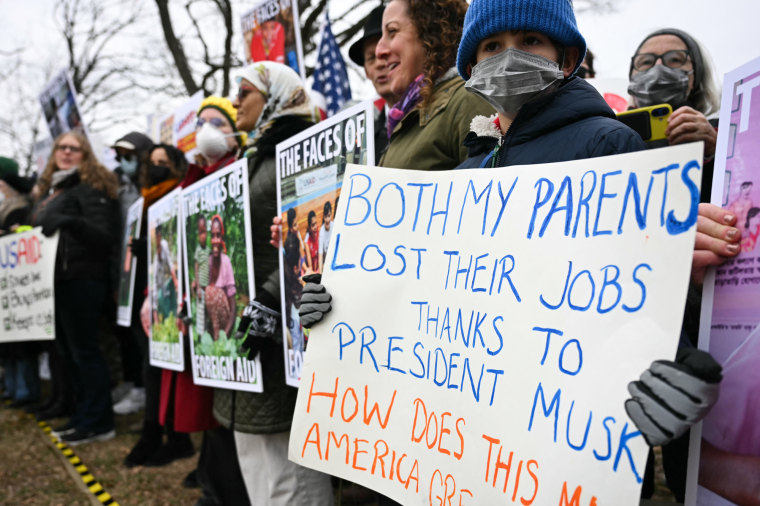 A boy holds a sign saying "Both my parents lost their jobs thanks to President Musk"