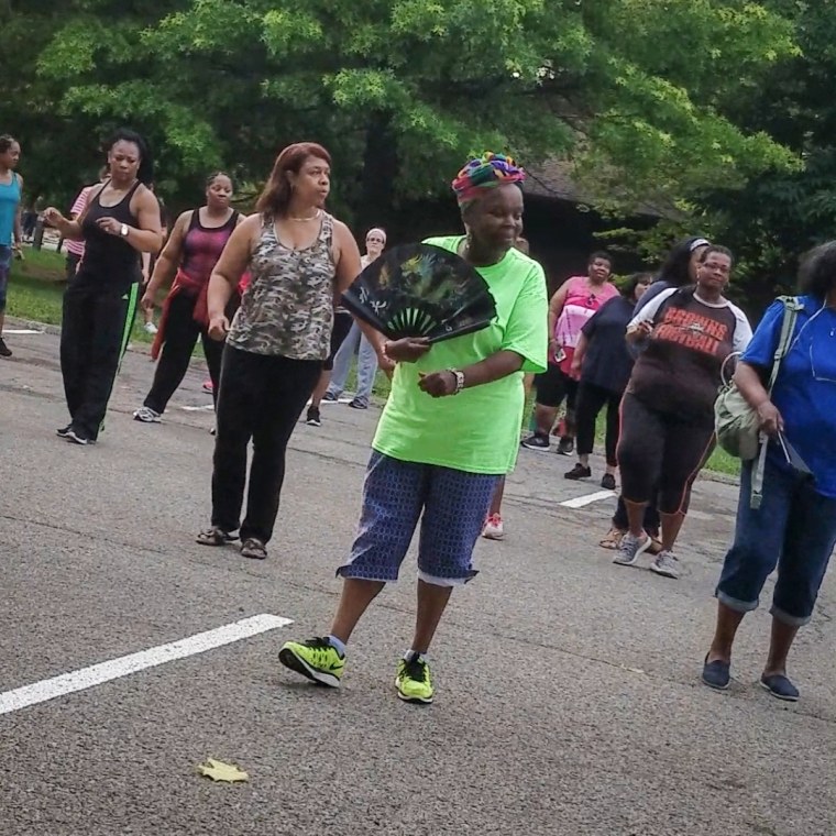 An older woman line dances in a parking lot with other women