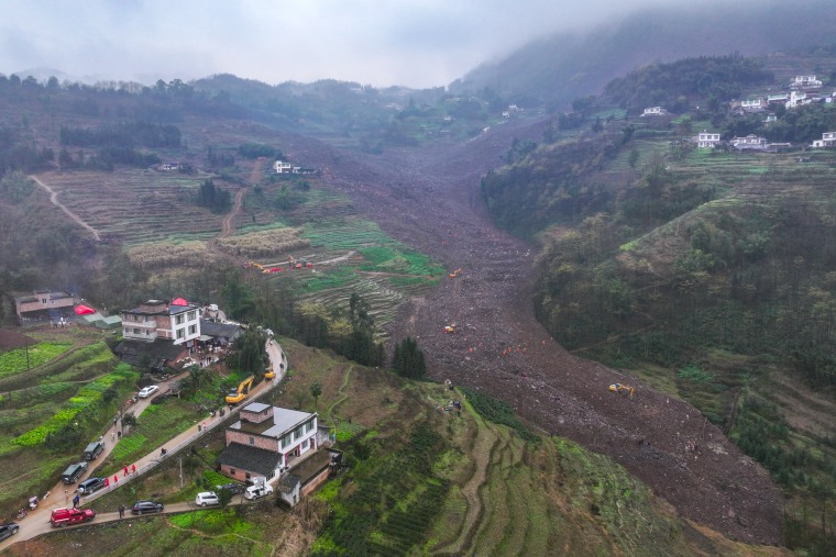 Wide landscape view of rescuers and excavators working at a landslide-hit area