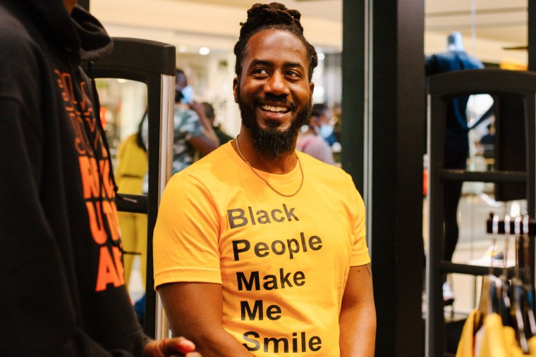 A man smiles wearing a yellow t-shirt that says "Black People Make Me Smile"