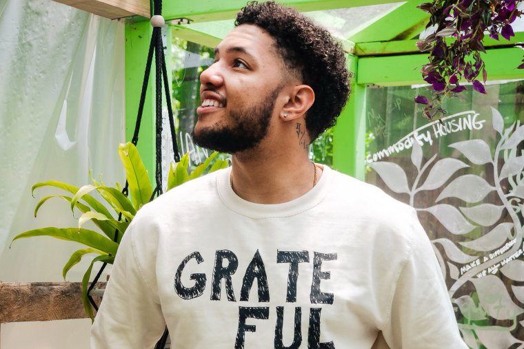 A man wears a beige sweatshirt that says "Grateful" in black text