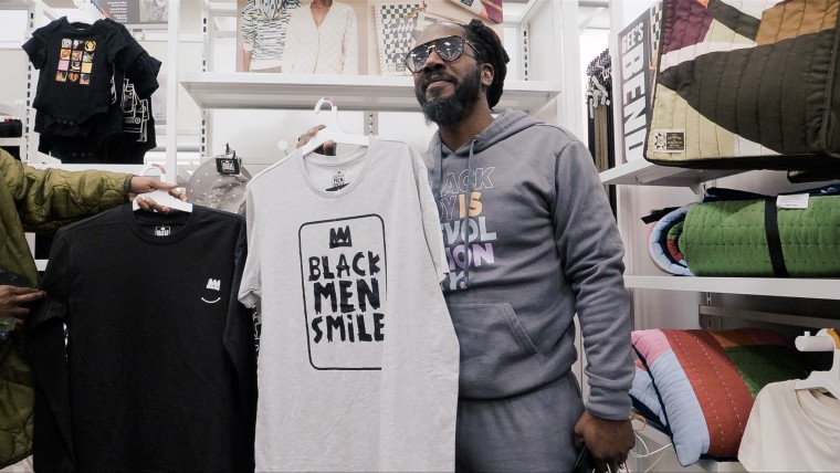 Carlton Mackey poses near his "Black Men Smile" t-shirt