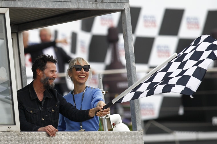 Keanu Reeves and Alexandra Grant wave the checkered flag at the MotoGP of Germany at the Sachsenring Circuit on July 7, 2024 in Hohenstein-Ernstthal.
