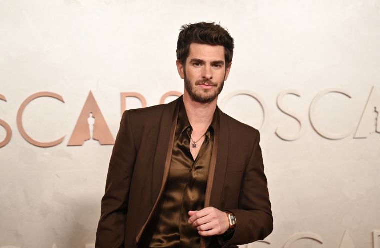 He's working late, cause he's an actor— Andrew Garfield stuns in an espresso suit.