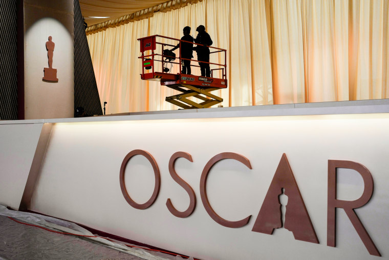 People stand in a lift above a wall with text that reads "Oscar"