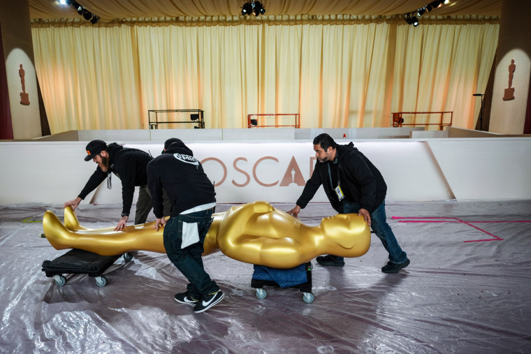 People wheel a large Oscar statue across a tarp floor