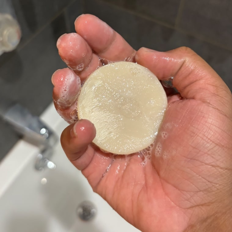 Person holding soapy Leaf shave bar in hand in the shower.