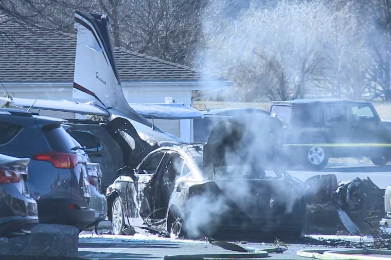 A damaged car in a parking lot next to a piece of plane debris