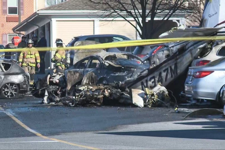 A damaged car in a parking lot next to a piece of plane debris