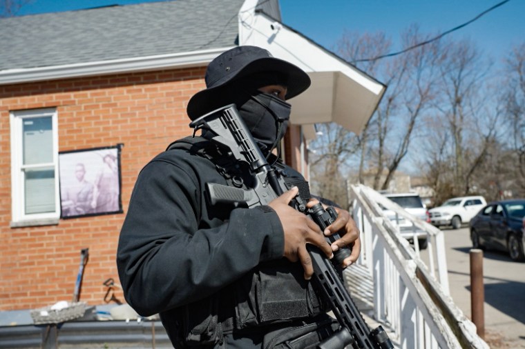 An armed volunteer for the Lincoln Heights Safety and Watch Program stands guard near a community center.