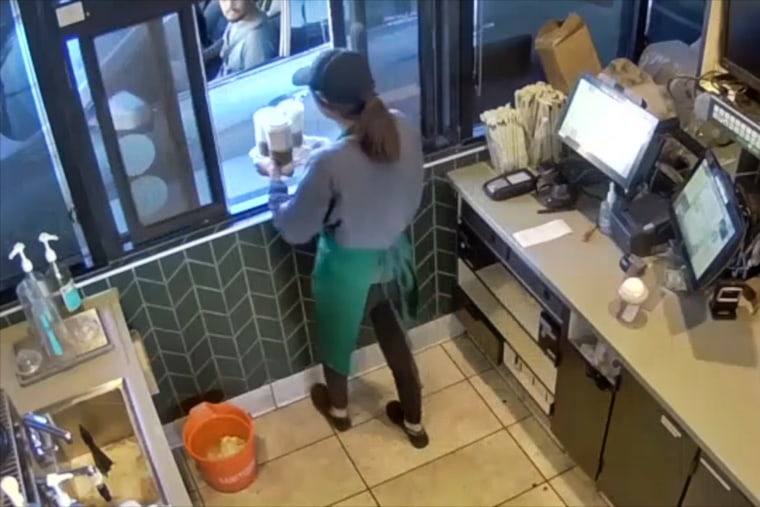 A Starbucks barista passes three coffee cups in a drink carrier through a drive through window to Michael Garcia who is seated in the front seat of his car