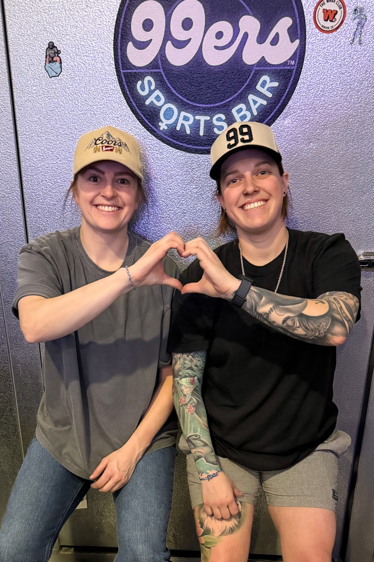 Annie Weaver, on the left, and Miranda Spence sit together and smile while forming a heart with their two hands