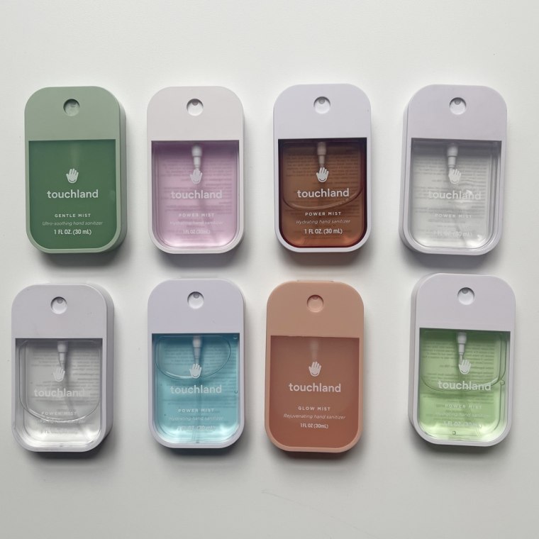 Eight Touchland hand sanitizers lay flat on a table in 2 rows, with four at the top and four at the bottom.