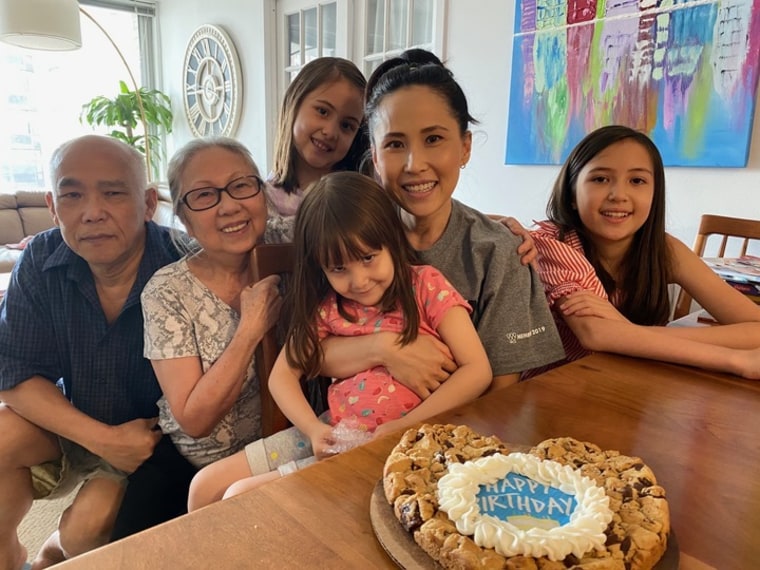 Photo of a family of six, seated at a table with a birthday cake on it.