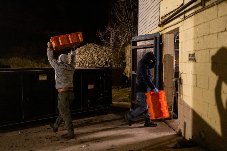 Farm workers dump out discarded mushroom pieces into a dumpster outside