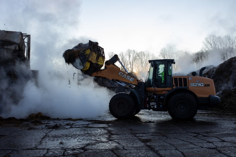 A person operates a wheel loader outside on a farm