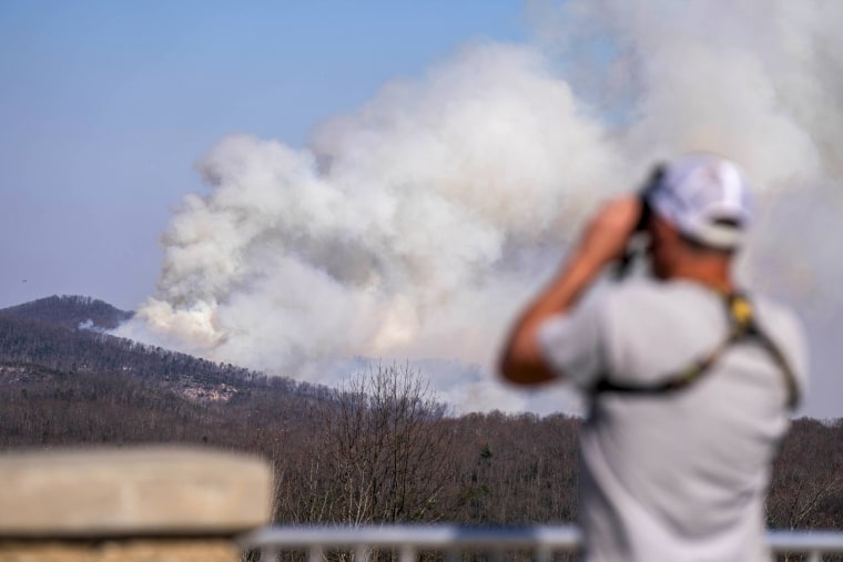 A man uses binoculars as smoke rises.