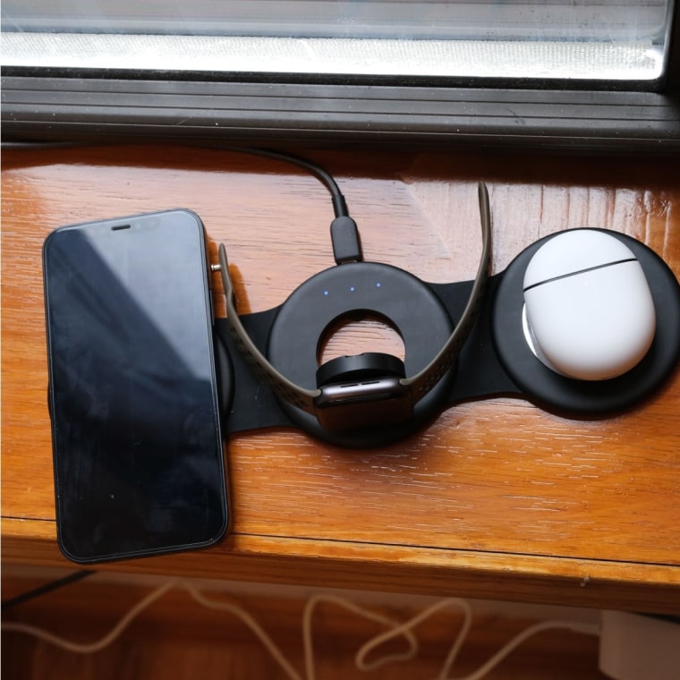 An iPhone, Apple Watch and earbuds case sitting on the Hicober charger on a windowsill.