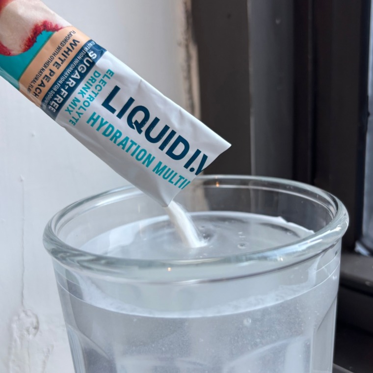 Person pouring packet of electrolyte powder into a cup of water.