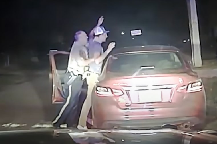 Shane Iverson, left, is pressing Michael Randall up against a vehicle and moving both of Michael's arms up in the air