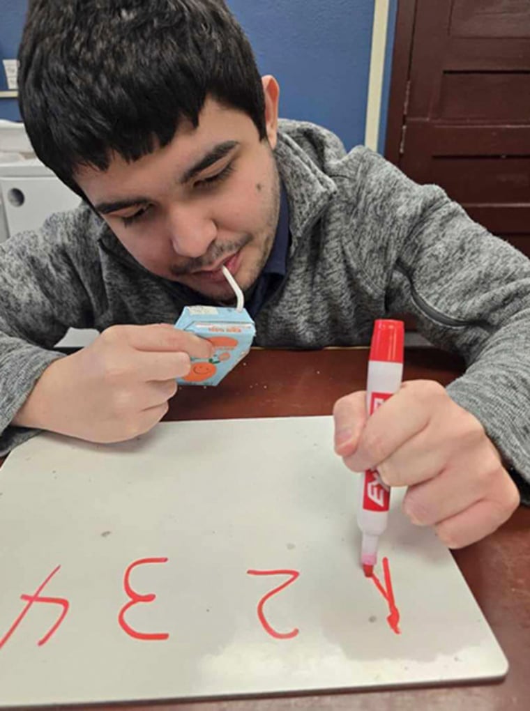 Victor Perez sips on a juice box and uses a red marker to write on a dry erase board